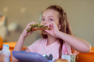 Uzun saçlı kız öğrenci okulda öğle yemeği için sandviç yeme