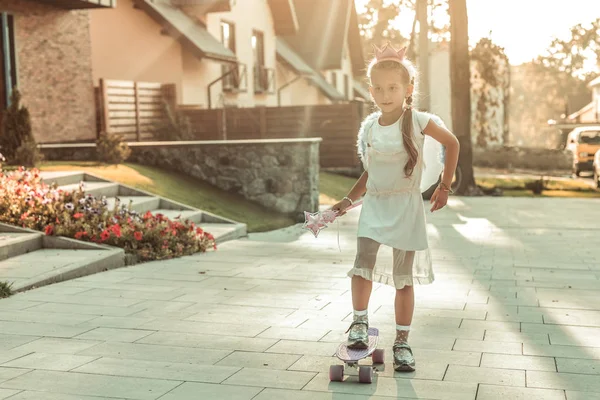 Resolute young lady in white dress riding on a skateboard — Stock Photo, Image