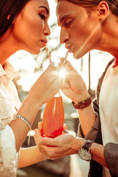 Atenta pareja atractiva sosteniendo vidrio con bebida naranja — Foto de Stock