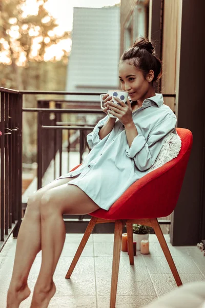 快適なアームチェアのバルコニーに座ってかなり黒髪のアジアの女の子 — ストック写真