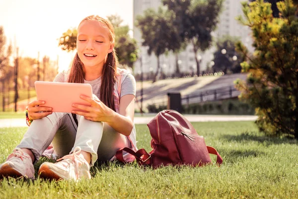 Sorrindo jovem senhora refrigeração em uma grama verde e verificando tablet — Fotografia de Stock