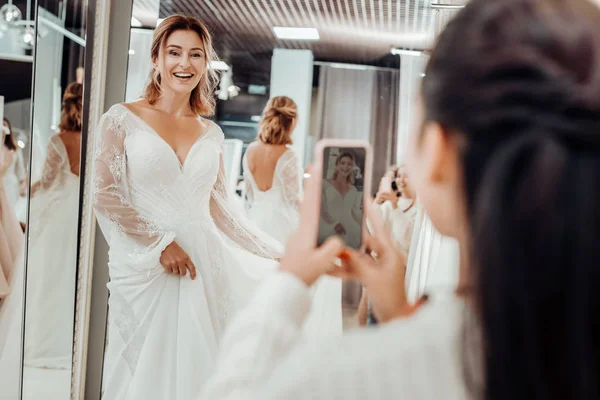 Bridesmaid taking pictures of her friend in wedding dress.