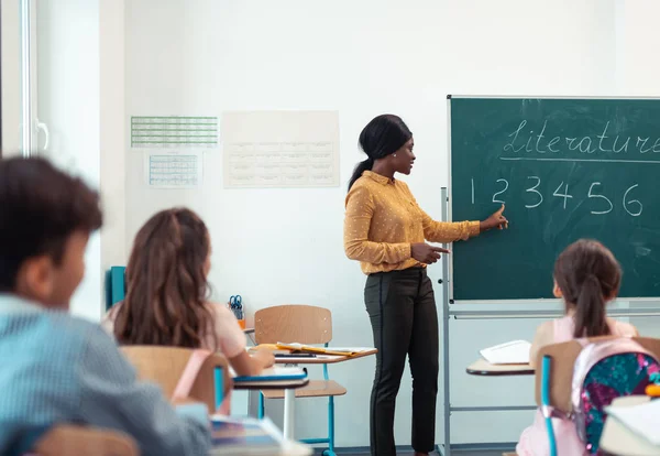 Dark-haired teacher standing near the blackboard