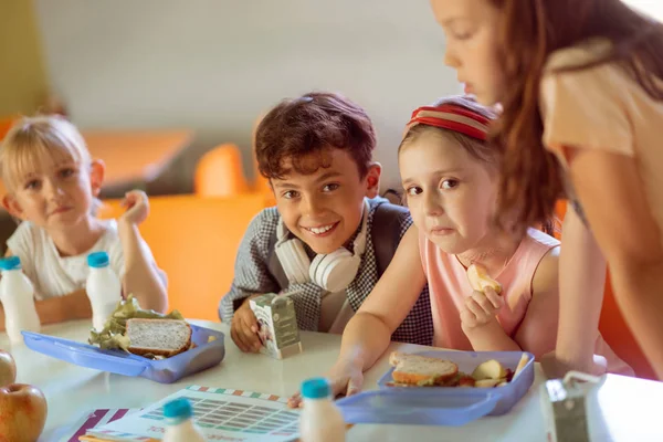 Niño sonriendo mientras está sentado cerca de las niñas almorzando juntos —  Fotos de Stock