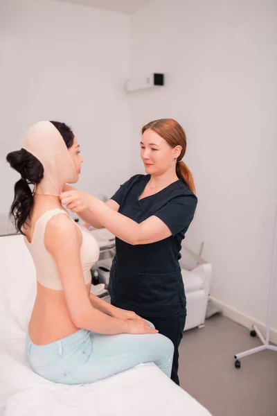 Krankenschwester legt nach chirurgischer Korrektur Verband auf Gesicht des Klienten — Stockfoto