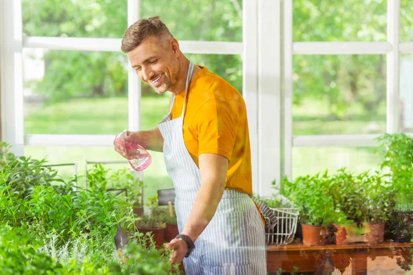 Hombre sonriente rociando plantas en su floristería . — Foto de Stock