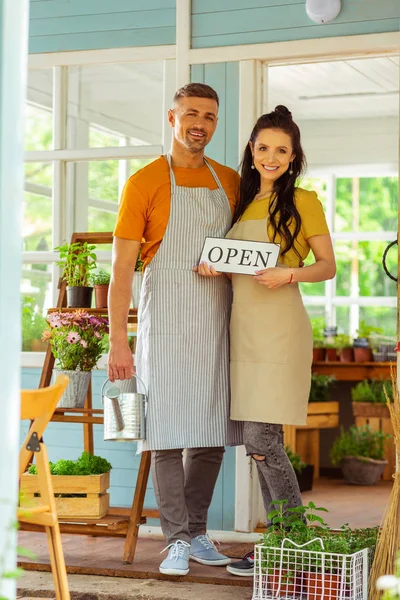Happy couple with an open sign standind near flower shop. — Stock Photo, Image