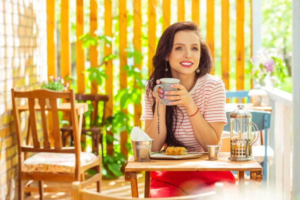 Mujer sonriente tomando café en una terraza de un café . — Foto de Stock