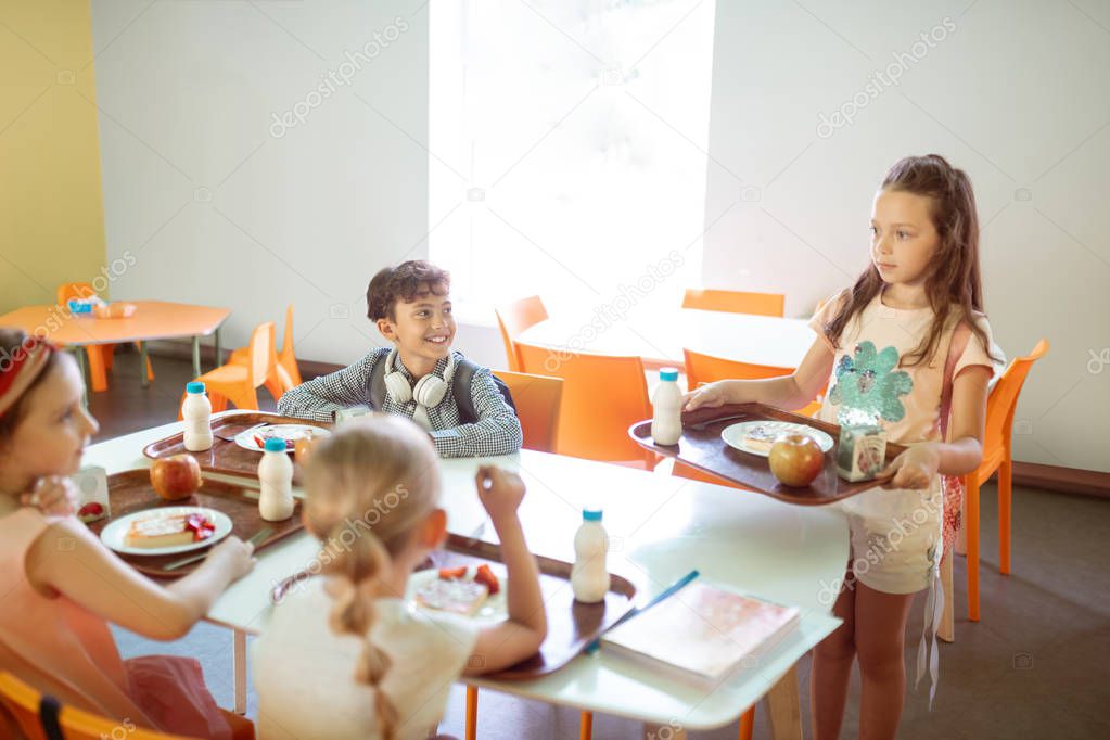 Dark-haired girl joining her friends in the school canteen