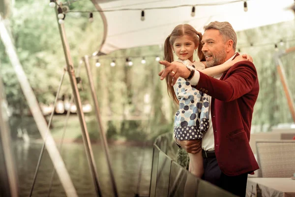 Отец держит свою дочь, глядя на уток в озере — стоковое фото