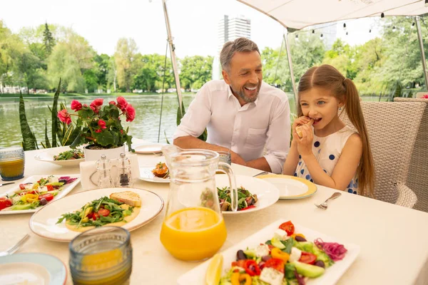 Nonno dai capelli grigi che sorride guardando la ragazza mangiare bruschette — Foto Stock