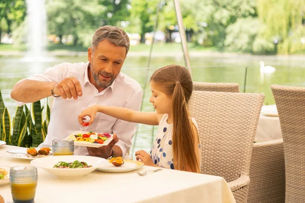 Schattig donkerharige meisje eten lekkere Griekse salade met grootvader — Stockfoto