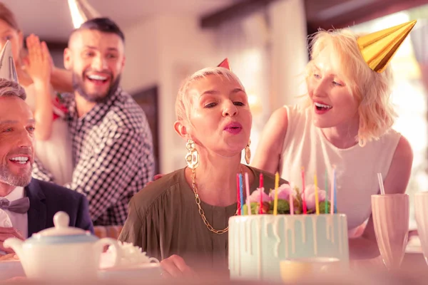 Aged woman blowing at candles celebrating birthday with family