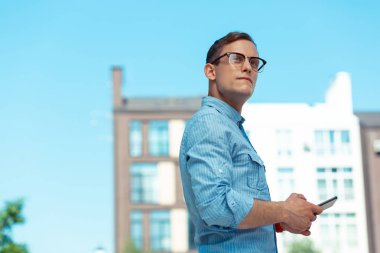 Yakışıklı koyu saçlı genç adam şehir blokları yakınında yürüyor