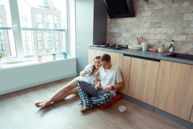 Dizüstü bilgisayarda çalışan kocasının yanında yerde oturan kadın