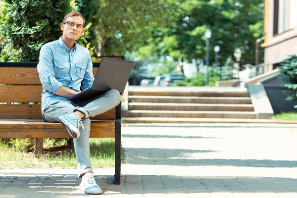 Guapo freelancer elegante sentado en el banco con el ordenador portátil —  Fotos de Stock