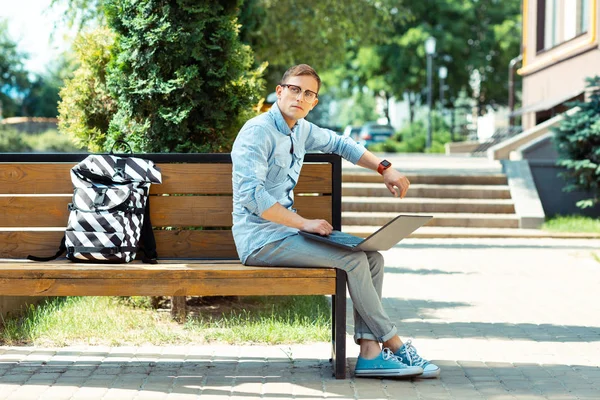 Ελεύθερος επαγγελματίας φορώντας έξυπνο ρολόι κάθεται έξω δουλεύοντας σε φορητό υπολογιστή — Φωτογραφία Αρχείου