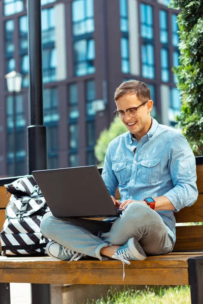 Dark-haired IT specialist working outside sitting on the bench