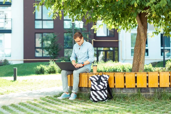 Dark-haired IT specialist wearing glasses working on laptop outside