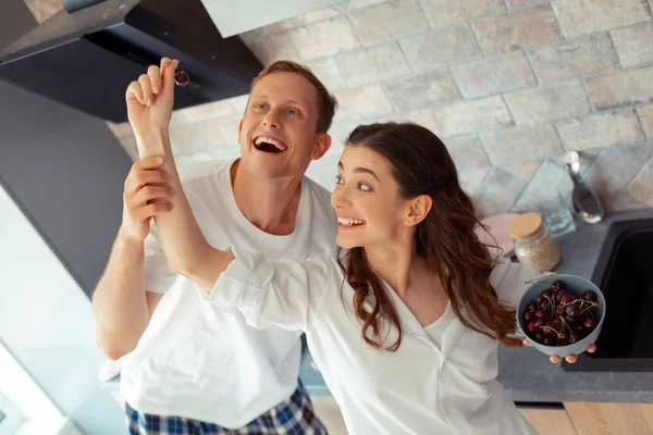 Pareja vistiendo pijamas divirtiéndose comiendo cerezas para el desayuno — Foto de Stock