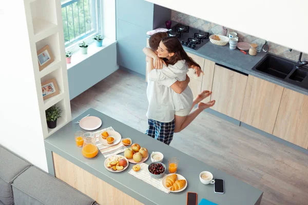 Dark-haired husband lifting his happy wife in the kitchen