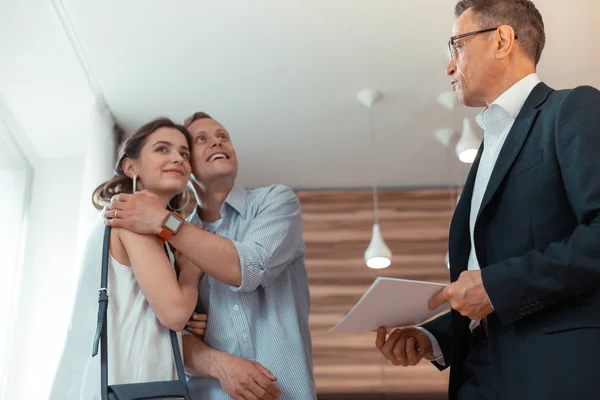 Esposo abrazando esposa después de comprar casa de pie cerca de agente inmobiliario — Foto de Stock