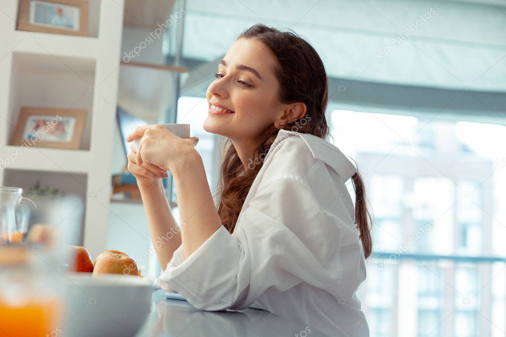 Woman wearing white shirt feeling relaxed drinking coffee