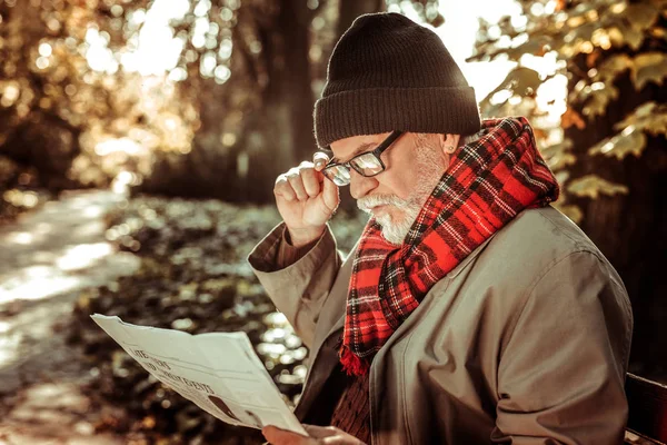 Bärtiger älterer Mann sitzt mit Zeitung auf der Bank. — Stockfoto