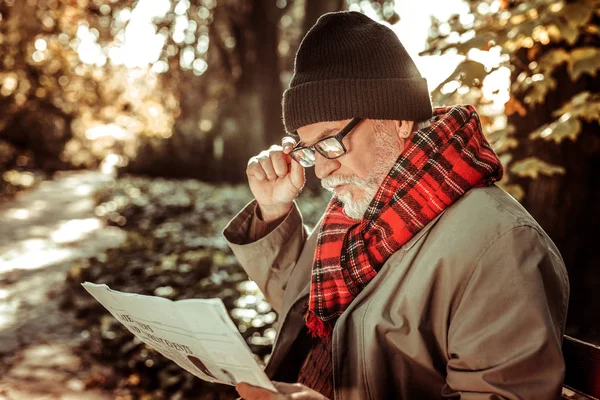 Vousatý starší muž sedící na lavičce s novinami. — Stock fotografie