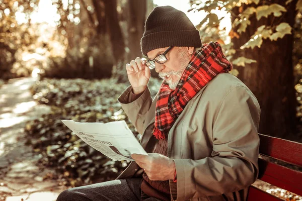 Hombre mayor concentrado leyendo atentamente un periódico . — Foto de Stock