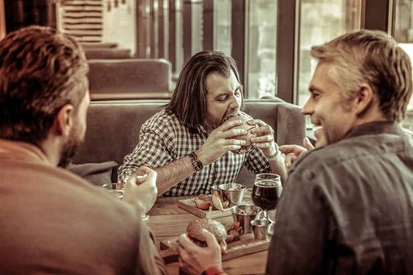 Éhes longhaired ember étkezési Burger örömmel — Stock Fotó