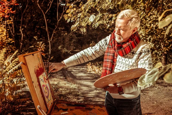 Äldre man målning en bild på ritningen staffli. — Stockfoto