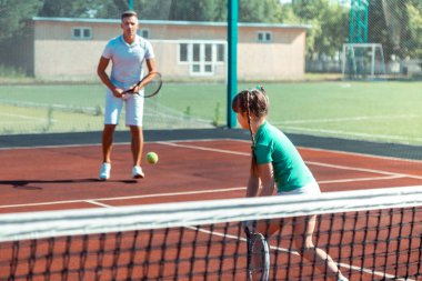 Beyaz tişört ve şort giyen baba kızıyla tenis oynarken