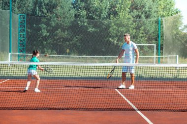 Babasıyla tenis oynarken koşan koyu saçlı kız