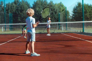 Curly son holding tennis racket while playing tennis clipart