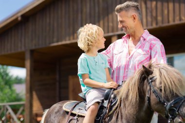 Kıvırcık sarı saçlı oğlu at üzerinde oturan ve babası yla konuşurken
