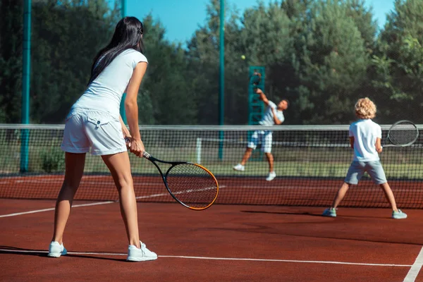 Темноволосая жена играет в теннис с мужем и сыном — стоковое фото