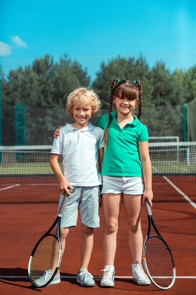 Curly blonde brother standing near sister standing on tennis court — Stock Photo, Image