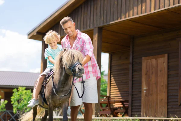 Grijs harige knappe vader neemt zijn zoon voor een paardenrit — Stockfoto