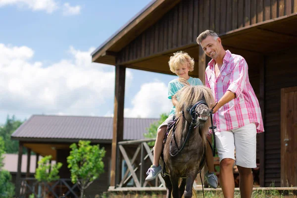 Pai sentindo-se memorável enquanto filho montando pouco cavalo marrom — Fotografia de Stock