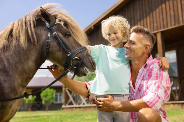 Vader en zoon staan in de buurt van goed uitziende bruine paard — Stockfoto