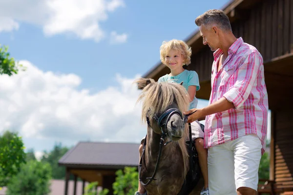 Dark-eyed curly son feeling happy riding horse for the first time