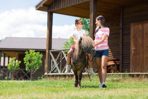 Mère brune enseignant à sa fille à monter à cheval — Photo