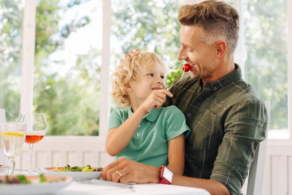 Cute curly blonde-haired son giving tomato to his father