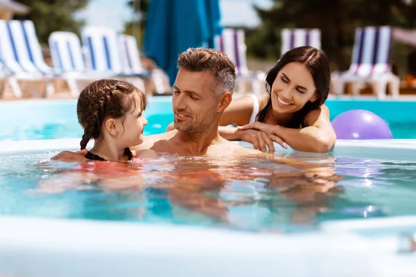 Hija sintiéndose feliz nadando en la piscina con los padres — Foto de Stock