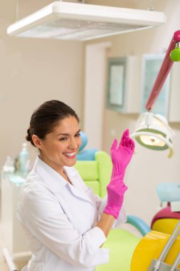 Güzel gülümseyen koyu saçlı doktor aseptik eldiven koyarak