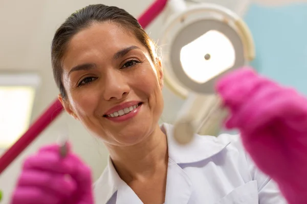 Smiling friendly dark-haired female dentist holding dental instruments