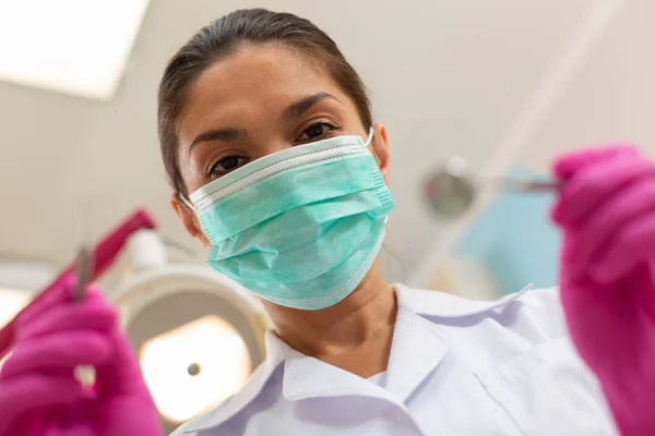 Allvarlig brunögda kvinna tandläkare i en grön mask — Stockfoto