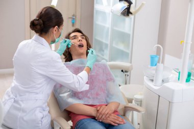 Diş hekimi erkek hastalarının dişlerini diş teli ile kontrol ediyor