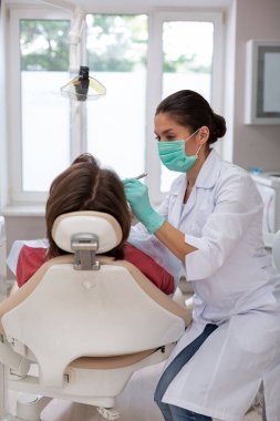 Kadın diş hekimi bir erkek hastaya dikkatle bakıyor